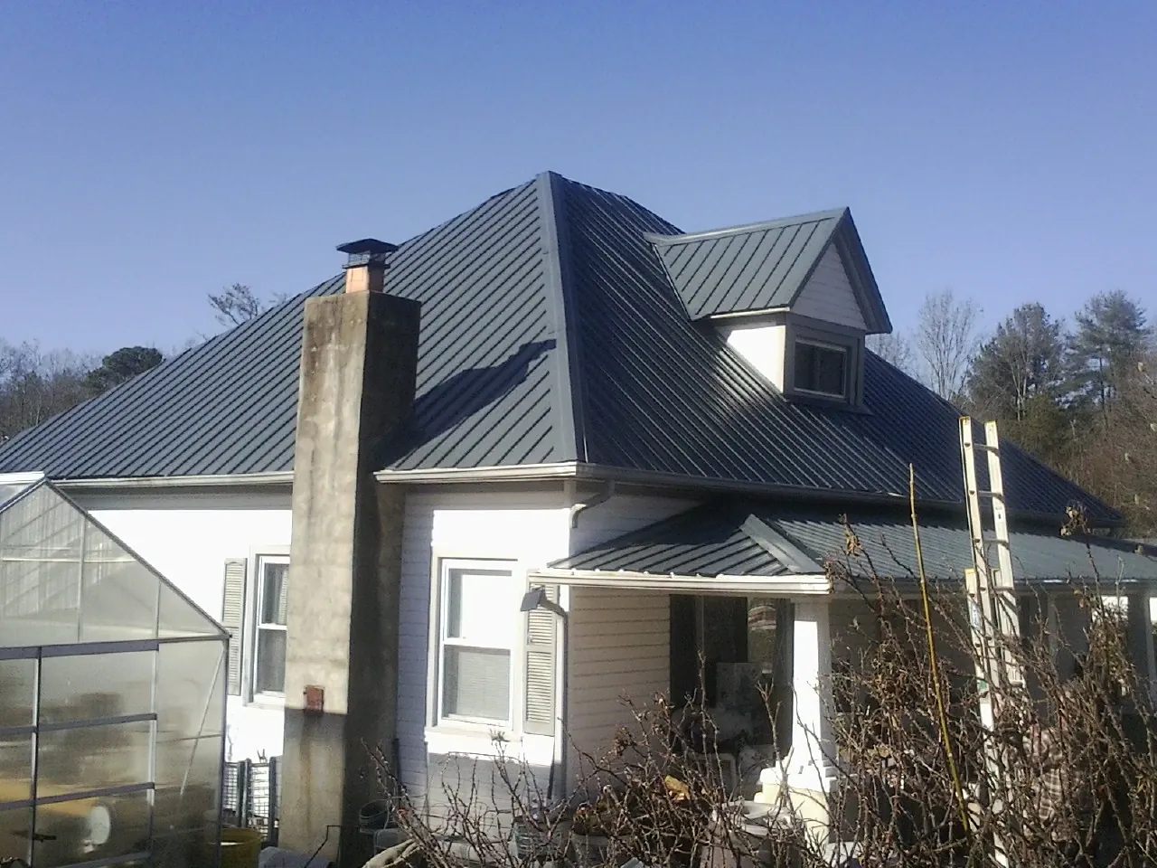 Dark blue standing seam metal roof on a white farmhouse with dormer — Slate & Tile Roof Repair by Roofing Brothers in Sandy Ridge