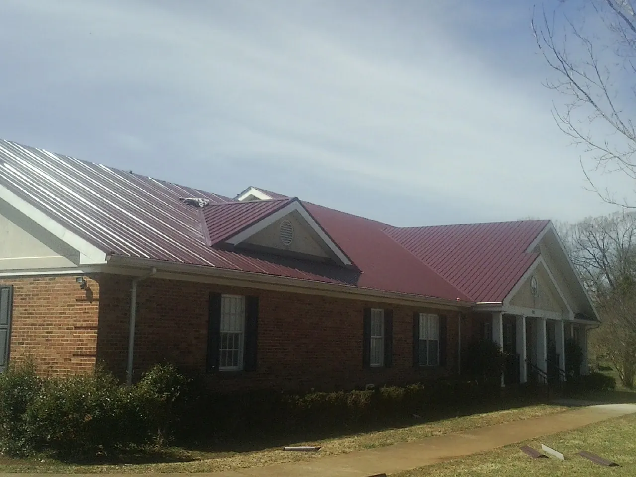 Red metal roof with gabled entries on a long brick building, from a Hail Damage Roof Repair job in Sandy Ridge