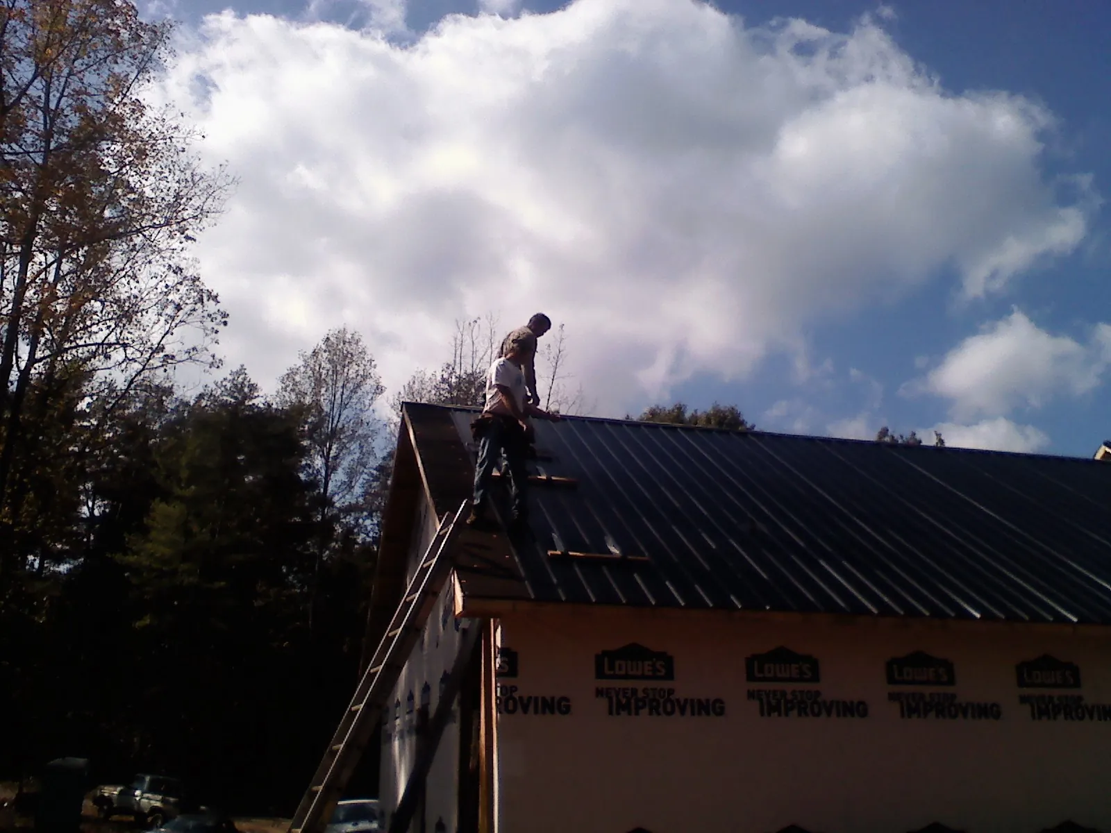 Roofer fastening dark metal panels high against a cloudy sky, from a Roof Inspection job in Sandy Ridge