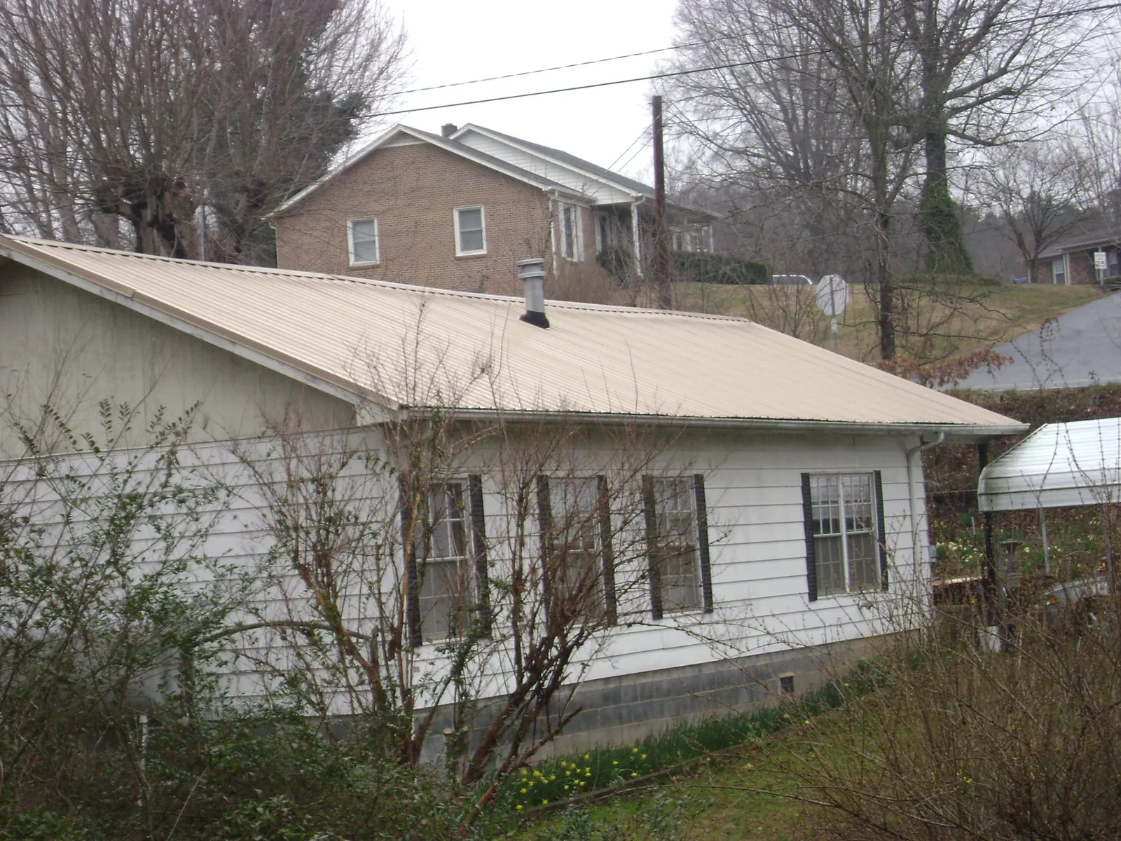 Tan metal roof on a white sided house set into a hillside — Commercial Roofing by Roofing Brothers in Sandy Ridge