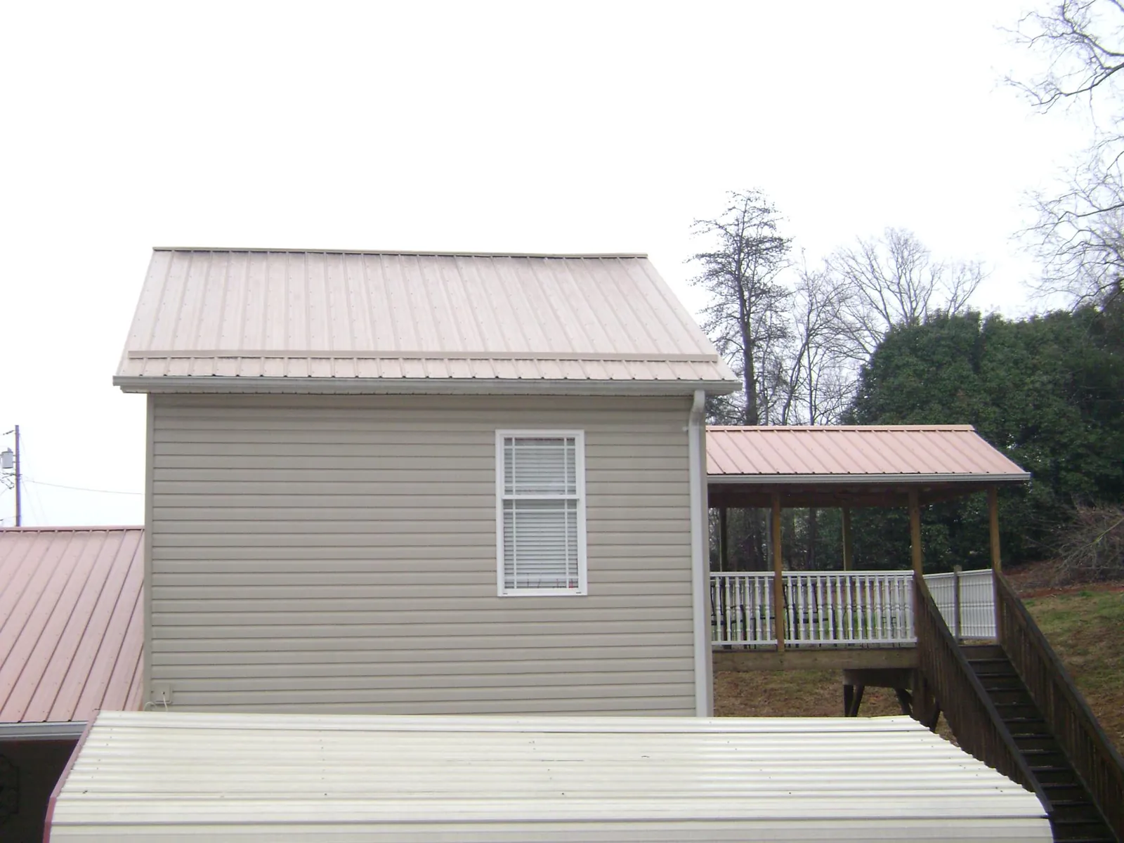 Tan metal roofs on a two story addition and attached porch, from a Roof Replacement job in Sandy Ridge
